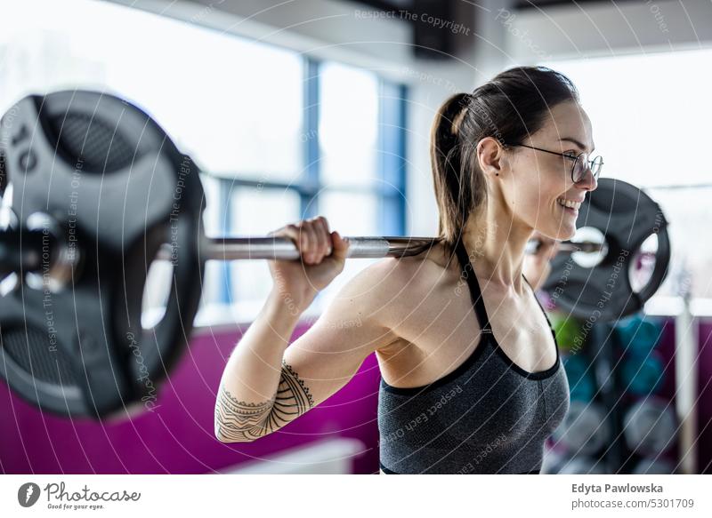 Junge Frau trainiert mit einer Langhantel im Fitnessstudio Wellness Wohlbefinden Bodybuilder sportlich Heben Bizeps Muskeln Curl-Hantel Bodybuilding Menschen