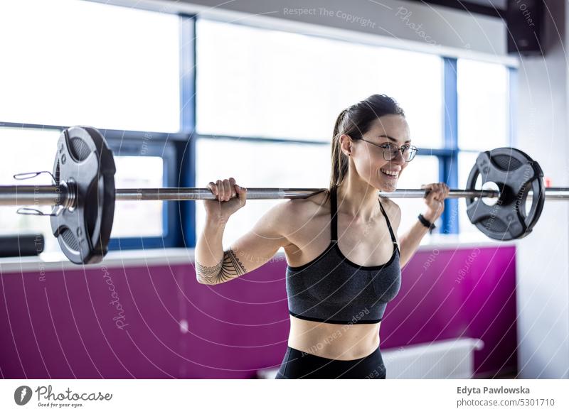 Junge Frau trainiert mit einer Langhantel im Fitnessstudio Wellness Wohlbefinden Bodybuilder sportlich Heben Bizeps Muskeln Curl-Hantel Bodybuilding Menschen