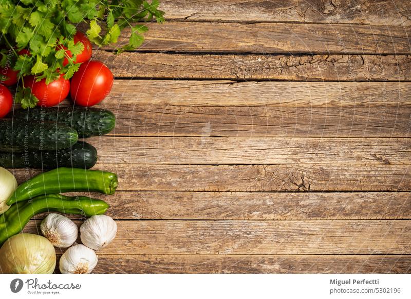 Gemüse für die Zubereitung von Gazpacho, Tomaten, Gurken, Zwiebeln, Knoblauch, Paprika und Petersilie, auf einer Seite des Fotos, das Platz für Texte lässt, auf einem rustikalen Holzhintergrund.