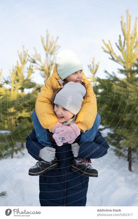 Glückliche Schwestern verbringen Zeit miteinander im Winterwald Zusammensein Geschwisterkind Kindheit Huckepack heiter Spaziergang warme Kleidung Lächeln Kinder