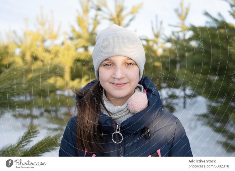 Zufriedenes Mädchen in warmer Kleidung schaut in die Kamera im Wald Winter Schnee warme Kleidung Feiertag Natur Baum Lächeln kalt Kind positiv Glück Kindheit