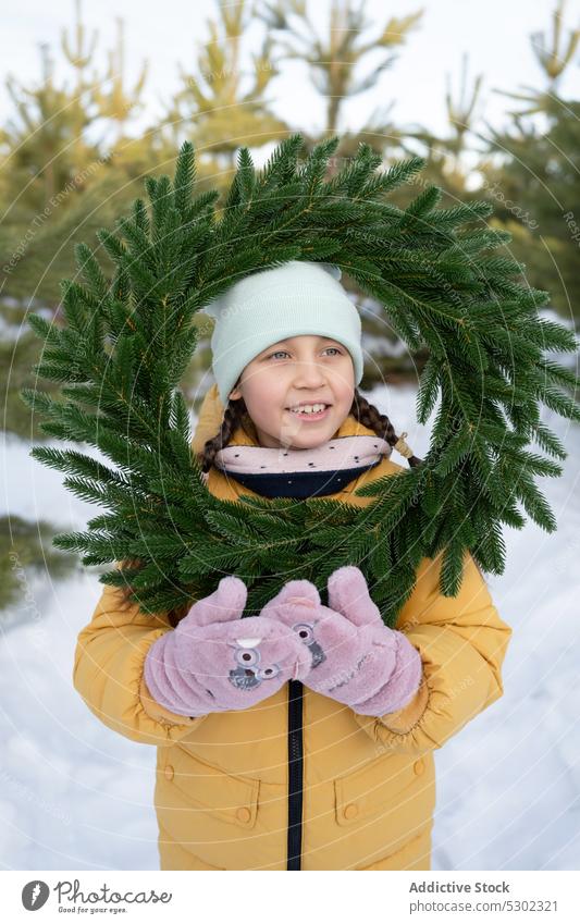 Niedliches Mädchen mit Kranz im verschneiten Wald Winter Natur Schnee Totenkranz warme Kleidung Lächeln nadelhaltig Hut kalt Wälder Saison Oberbekleidung Glück