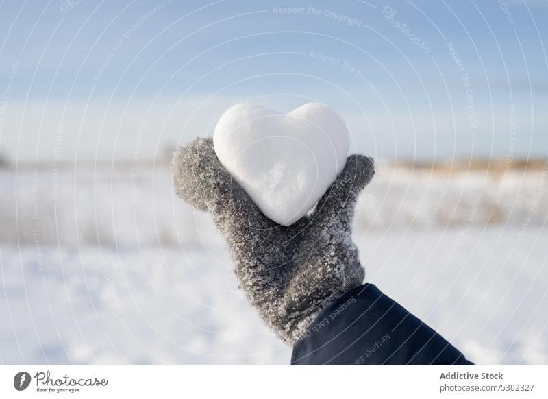 Anonyme Person mit herzförmigem Schneeball an einem Wintertag Herz zeigen manifestieren kalt Frost Natur warme Kleidung gefroren Winterzeit Boden Saison