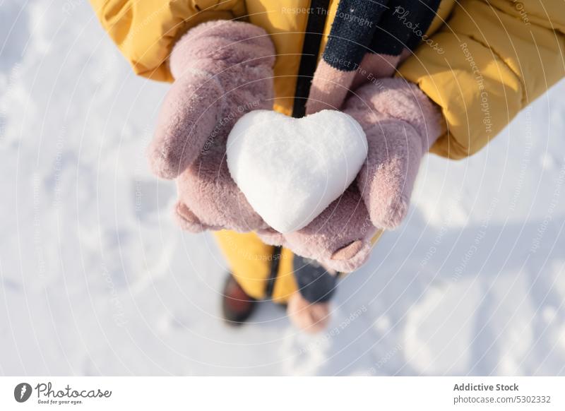 Anonyme Person mit herzförmigem Schneeball an einem Wintertag Herz zeigen manifestieren kalt Frost Natur warme Kleidung gefroren Winterzeit Boden Saison