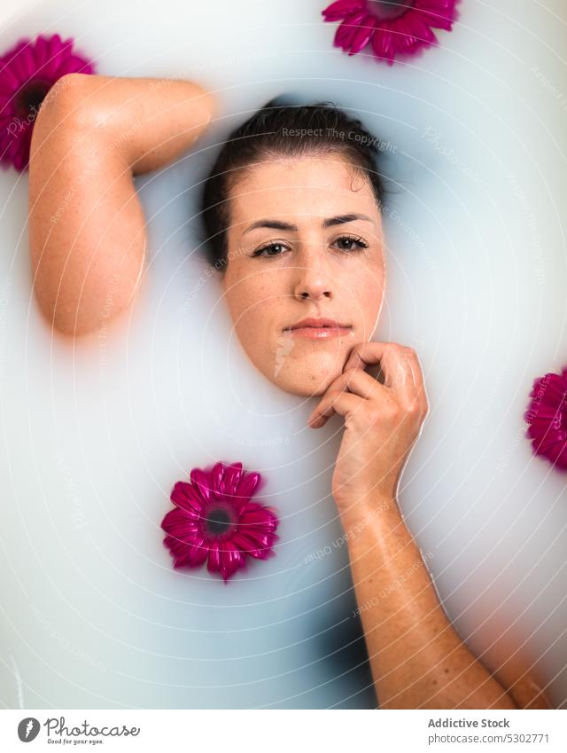 Zärtliche Frau, die ihr Gesicht berührt, während sie sich in der Badewanne mit Blumen und Milch entspannt Gesicht berühren melken Spa sinnlich Wellness Therapie