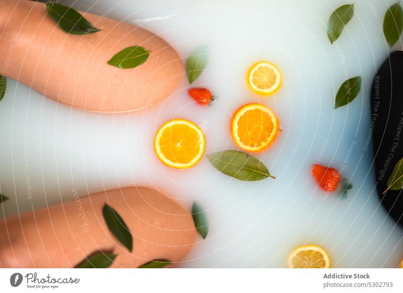 Crop Frau unter Milch Bad mit geschnittenen Orangen Erdbeeren und Blätter verjüngen Therapie Hydrat orange Scheibe melken Blatt Leckerbissen Gesundheit