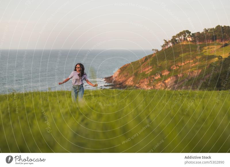 Glückliche Frau läuft auf grasbewachsenem Hügel in der Nähe des Meeres laufen Spaziergang bewundern MEER Natur malerisch friedlich reisen Lächeln lässig