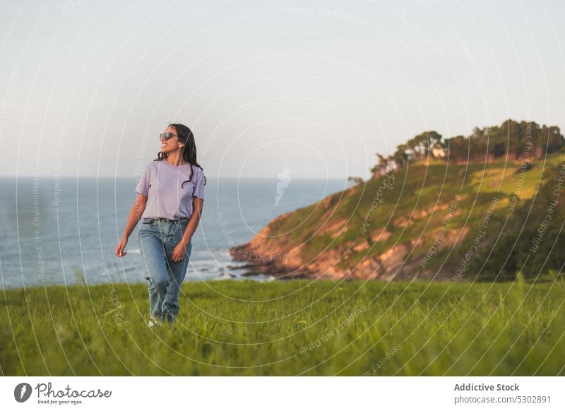 Glückliche Frau, die auf einem grasbewachsenen Hügel am Meer spazieren geht Spaziergang bewundern MEER Natur malerisch friedlich reisen Lächeln lässig