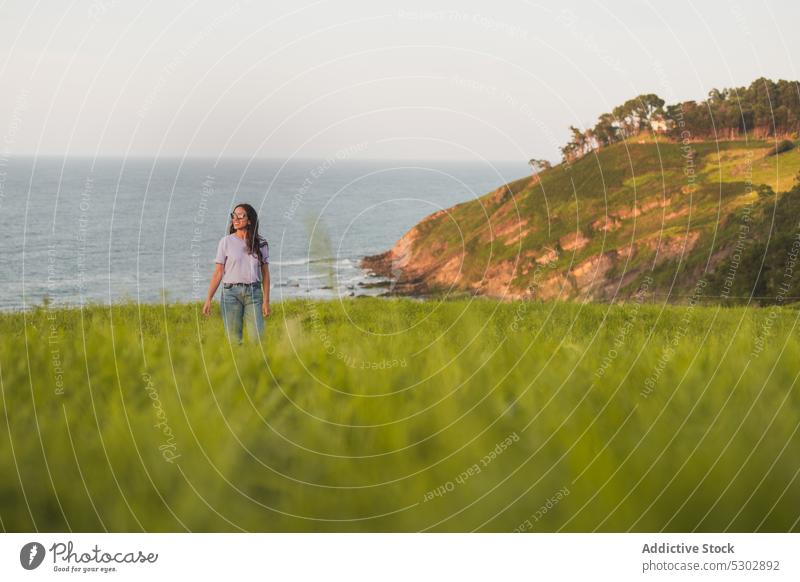 Glückliche Frau, die auf einem grasbewachsenen Hügel am Meer spazieren geht Spaziergang bewundern MEER Natur malerisch friedlich reisen Lächeln lässig