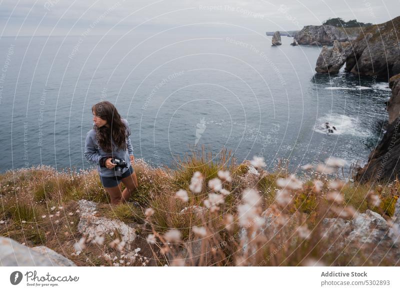 Weibliche Fotografin steht auf einer Klippe am Meer Frau reisen grasbewachsen professionell Fotoapparat Horizont endlos MEER jung Gerät tagsüber Fotokamera