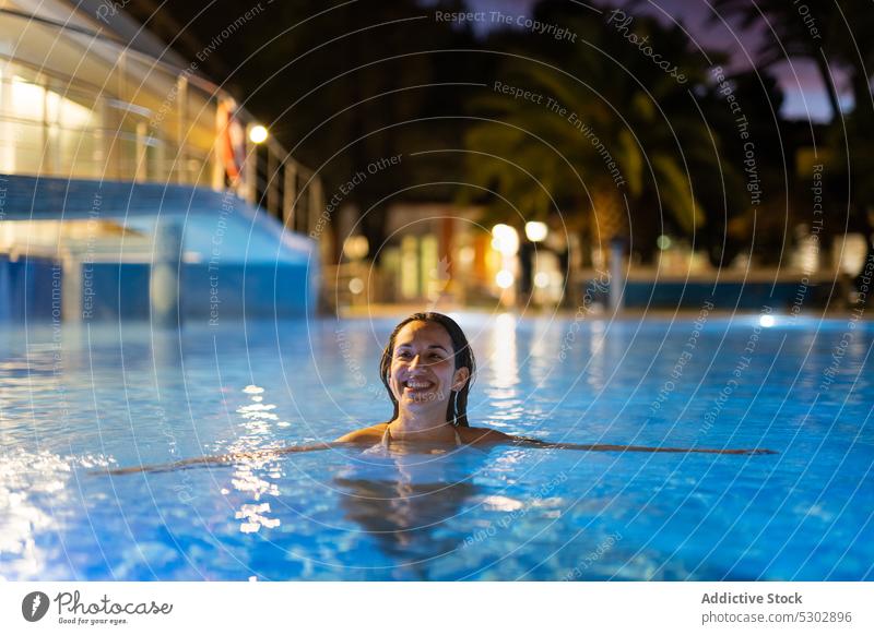 Fröhliche Frau schwimmt im Pool eines Ferienorts schwimmen Resort Glück heiter Urlaub Lächeln genießen Nacht Wasser Kälte jung ruhen Beckenrand
