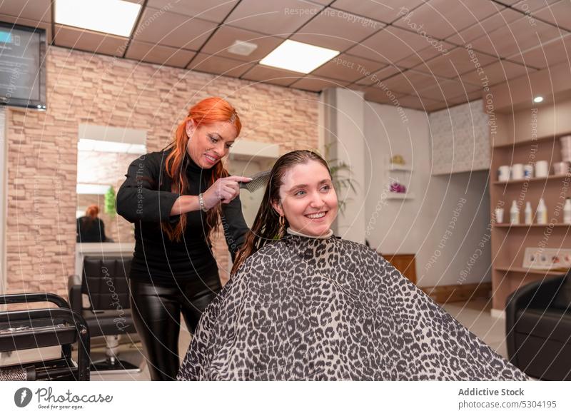 Fröhliche Friseurin kämmt das Haar eines Kunden Frauen Kamm Bürste Klient Frisur Salon Schönheit Verfahren Behaarung Lächeln professionell Meister positiv