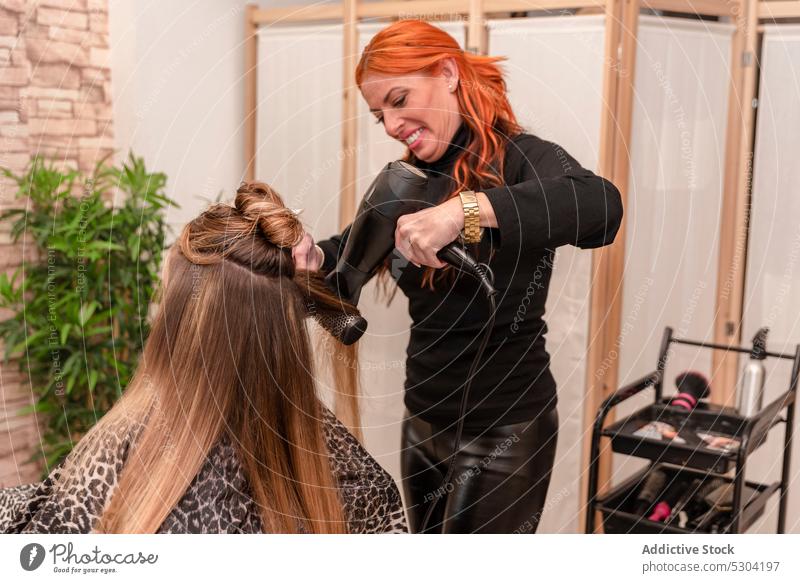 Positive Friseurin beim Trocknen der Haare eines Kunden Frauen Haartrockner Klient Salon Schönheit Bürste Verfahren Frisur trocknen Prozess professionell Stil