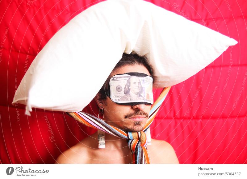 Es handelt sich um ein Fotokonzept über eine Person, die eine Augenbinde trägt, auf der ein Dollar steht, und auf deren Kopf ein Kissen befestigt ist. Netz Geld