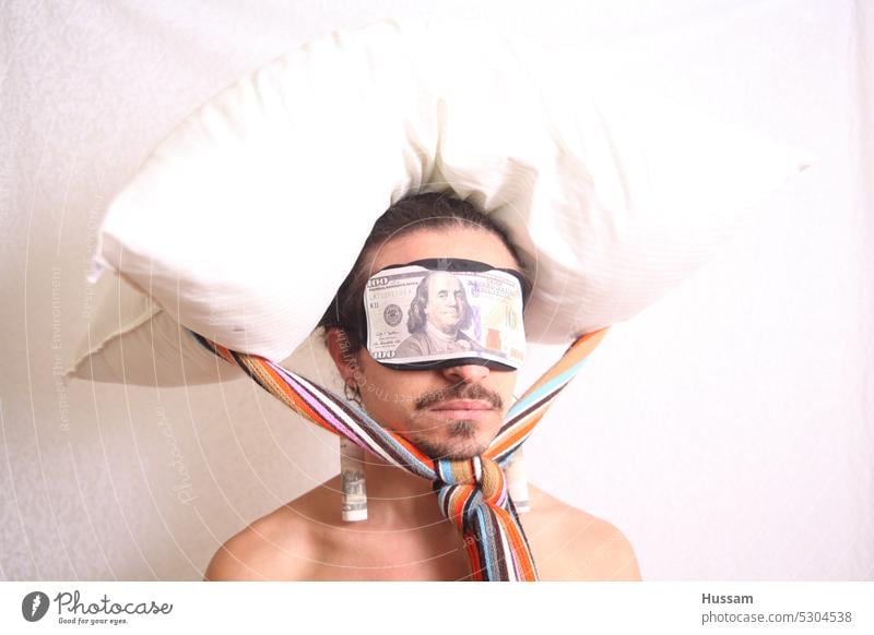 Es handelt sich um ein Fotokonzept über eine Person, die eine Augenbinde trägt, auf der ein Dollar steht, und auf deren Kopf ein Kissen befestigt ist. Inflation