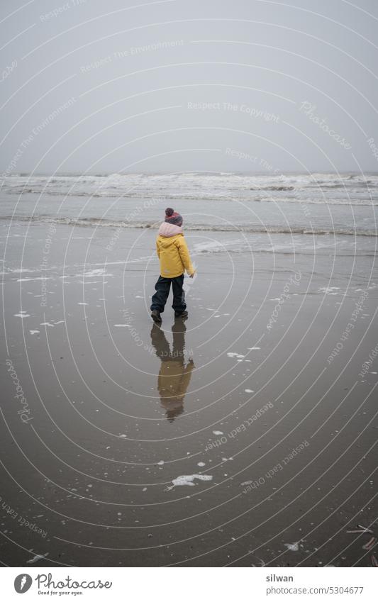Kind am spazieren am Watenmeerstrand bei windig-nass-nebligem Wetter Strand Sandstrand Nebel Wind kalt düster feucht Wellen Schaum grau weiss salzig moody rauh