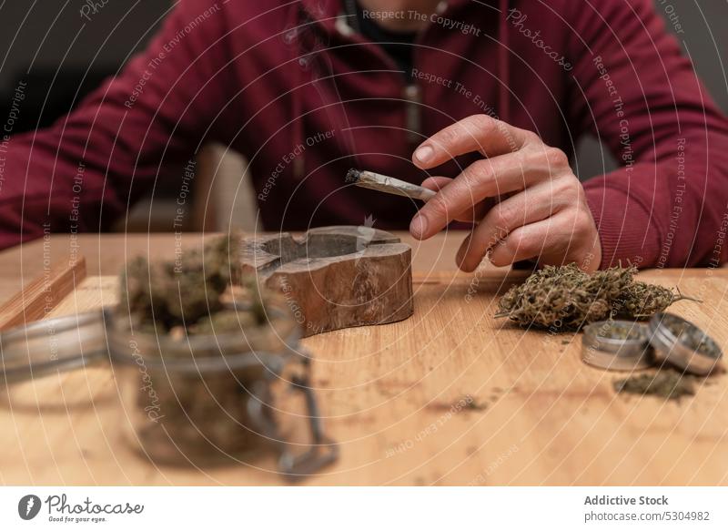 Crop-Mann sitzt am Tisch und raucht Cannabis Rauch Raucherin stumpf Kraut Marihuana Habitus legalisieren Medikament männlich Erwachsener Gelenk medizinisch