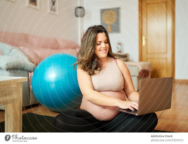 Glückliche schwangere Frau, die beim Training einen Laptop benutzt Lächeln Fitness Passform-Ball Pause Tippen heiter benutzend Bauch lange Haare Sportbekleidung