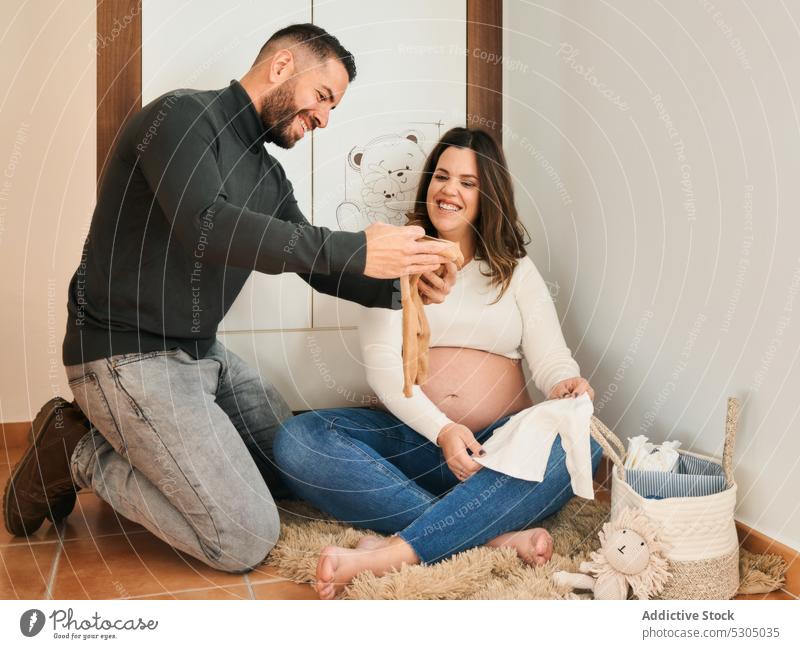 Freudiges werdendes Paar sieht sich Babykleidung an Ehefrau Ehemann schwanger erwarten Bauch mütterlich Kinderzimmer Lächeln froh Schwangerschaft Kinderkriegen