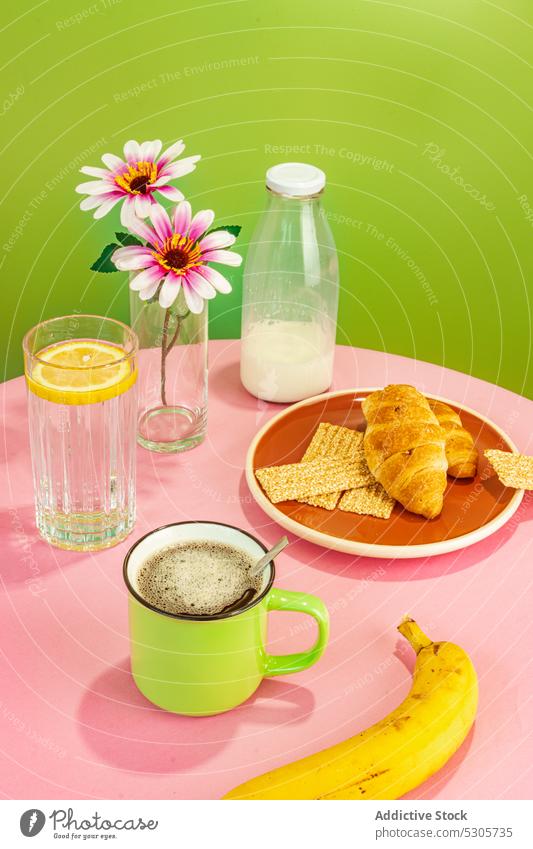 Leckeres Frühstück auf rosa Tisch Banane Blume Croissant Getränk Kaffee Wasser trinken melken Frucht Zitrone Vase frisch Tasse Flasche geschmackvoll lecker