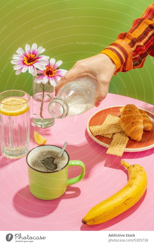 Eine Person gießt Milch in eine Tasse Kaffee Frühstück Croissant eingießen Getränk Morgen Blume melken Banane lecker Sahne frisch geschmackvoll trinken Vase süß