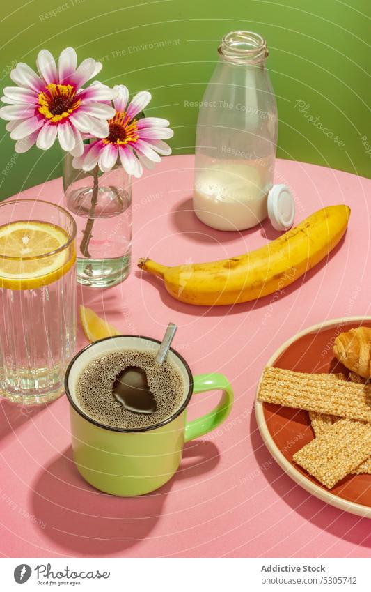 Leckeres Frühstück auf rosa Tisch Banane Blume Getränk Kaffee Wasser trinken melken Frucht Zitrone Vase frisch Tasse Flasche geschmackvoll lecker Blüte Morgen