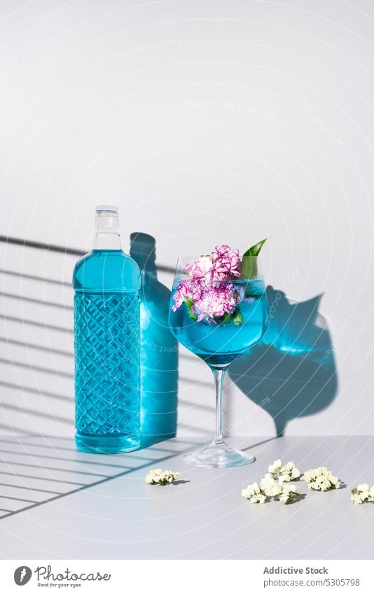 Erfrischender Cocktail mit Eiswürfeln bei Blumen und Flasche trinken Getränk blau Glas Alkohol Erfrischung kalt liquide Schatten Tisch Aperitif Blütezeit lecker