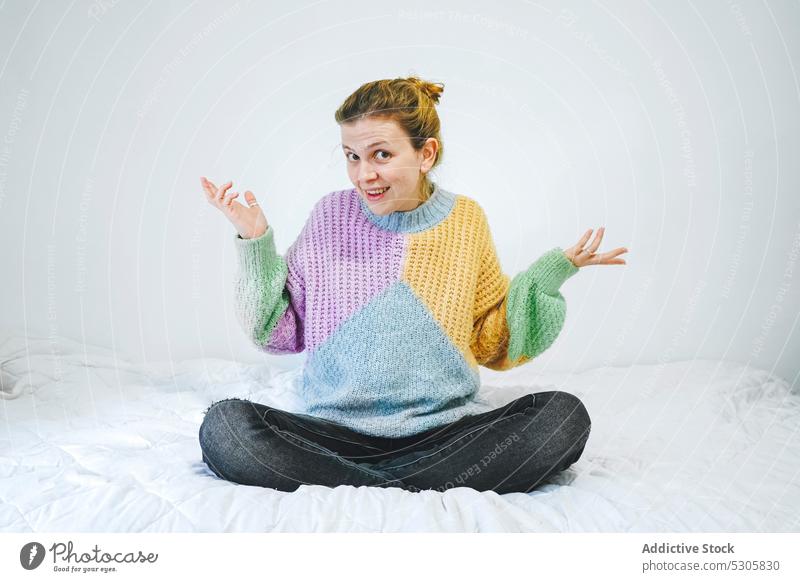 Verwirrte Frau in Lotus-Pose auf dem Bett Geduldsspiel verwirren Outfit heimwärts Schlafzimmer Pullover gestrickt lässig jung farbenfroh Stil Jeanshose