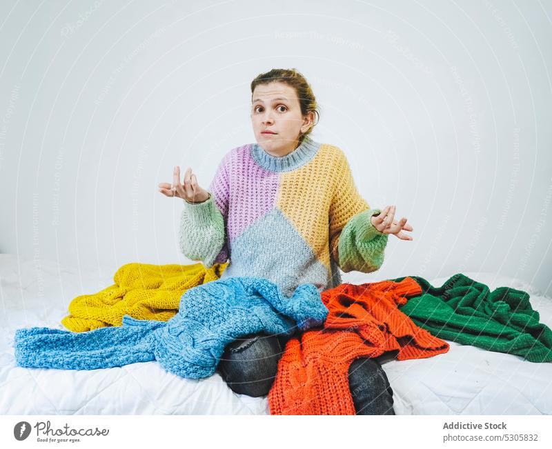 Verwirrte Frau mit bunten Pullovern schaut in die Kamera wählen Buch Bett verwirren heimwärts Komfort lässig besinnlich nachdenklich Strickwaren Stoff jung