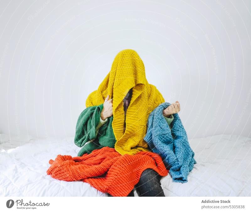 Anonyme Frau mit buntem Pullover bedeckt wählen Buch Bett verwirren heimwärts Komfort lässig besinnlich nachdenklich Strickwaren Stoff jung Schlafzimmer