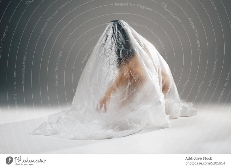 Anonyme Frau in Polyethylen eingewickelt auf dem Boden sitzend nackt anonym verschmutzen Desaster Umwelt Ökologie Müll umhüllen Zellophan hilflos Konzept