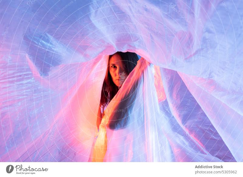 Frau schaut durch Plastikfolie in die Kamera Zellophan neonfarbig Licht Polyethylen verschmutzen Gefahr Kunststoff Filmmaterial Umwelt Desaster Ökologie