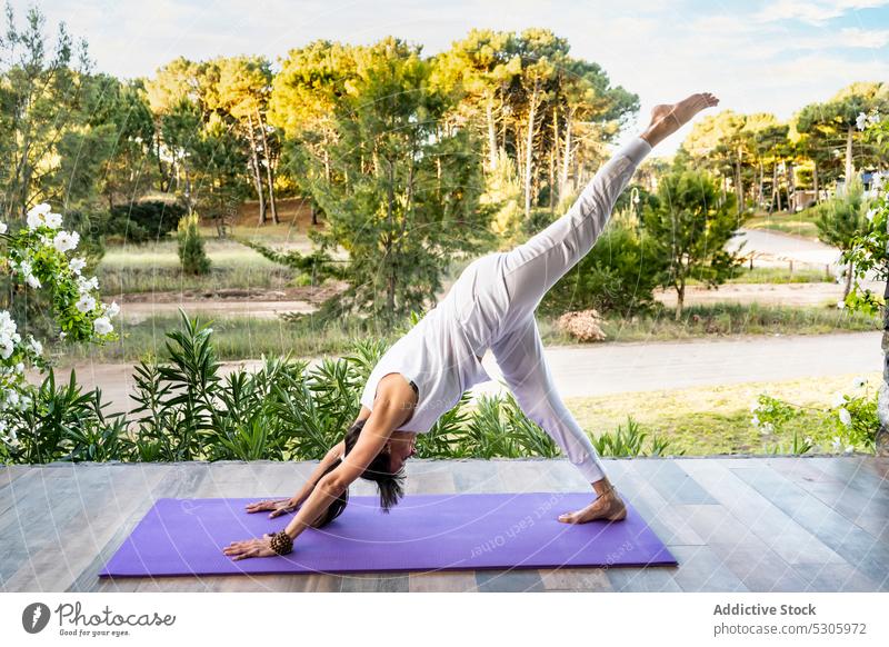 Konzentrierte Frau übt Yoga auf einer Matte in der Nähe eines Parks Asana stehende Spagate urdhva prasarita eka padasana beweglich meditieren Dehnung üben