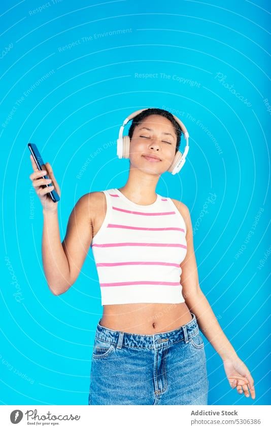 Fröhliche ethnische Frau, die über Kopfhörer Musik hört und tanzt Tanzen zuhören Smartphone Audio Gesang Wiedergabeliste Lächeln aufgeregt heiter Glück jung