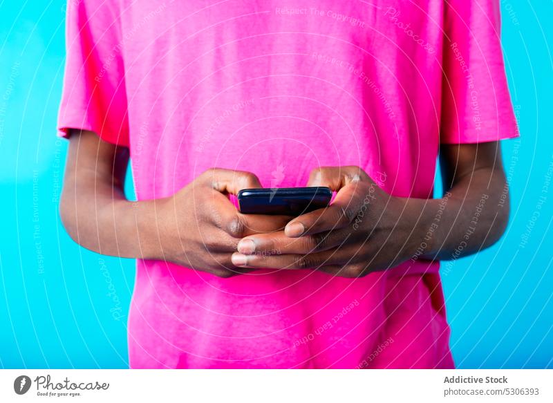 Anonymer schwarzer Mann mit Smartphone benutzend männlich jung Afroamerikaner ethnisch lässig hell farbenfroh Browsen Surfen Gerät Mobile Drahtlos Anschluss