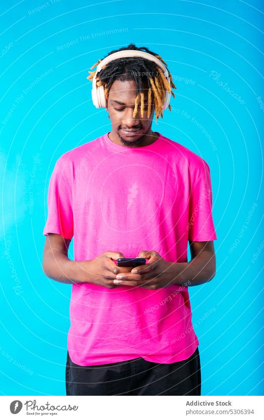 Schwarzer Mann hört Musik über Kopfhörer, während er sein Smartphone benutzt zuhören benutzend Audio Gesang Wiedergabeliste Melodie männlich jung Afroamerikaner