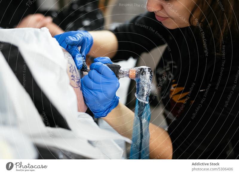 Konzentrierter Meister beim Tätowieren auf dem Arm eines Kunden Frau Mann Tattoo Klient Salon Maschine professionell Tusche Atelier Handschuh Verfahren Prozess