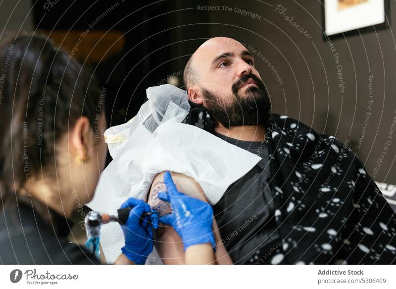 Konzentrierter Meister beim Tätowieren auf dem Arm eines Kunden Frau Mann Tattoo Klient Salon Maschine professionell Tusche Atelier Handschuh Verfahren Prozess