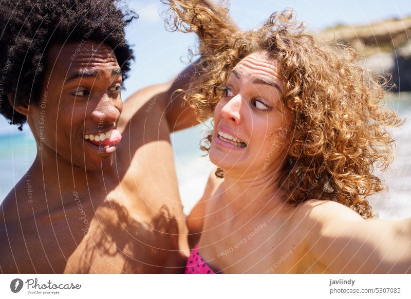 Selfie eines lustigen Paares, das am Strand Grimassen schneidet fotografieren ausspannen Zunge zeigen Gesicht machen Gesichtsausdruck Spaß haben Haare berühren