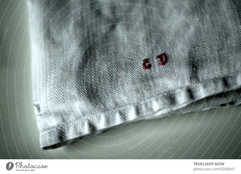 Küchentuch uralt mit gesticktem Monogramm auf Gewebestruktur in Nahaufnahme Struktur Stickerei Haushalt antik Textil Falten Licht und Schatten weiss grau