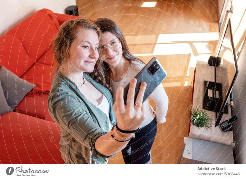 Lächelnde Frauen stehen und nehmen Selfie auf Smartphone zu Hause Freund positiv Zusammensein heiter benutzend Fenster Mobile Telefon Glück Apparatur Gerät jung