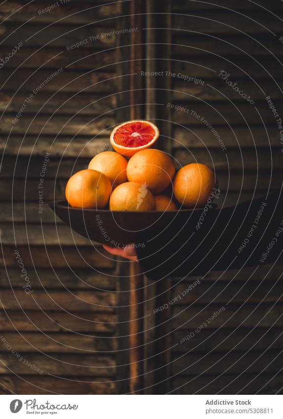 Reife rote Orangen in einer schwarzen Schale an einer Holzwand Person orange Schalen & Schüsseln reif Saft Frucht Zitrusfrüchte frisch Lebensmittel süß