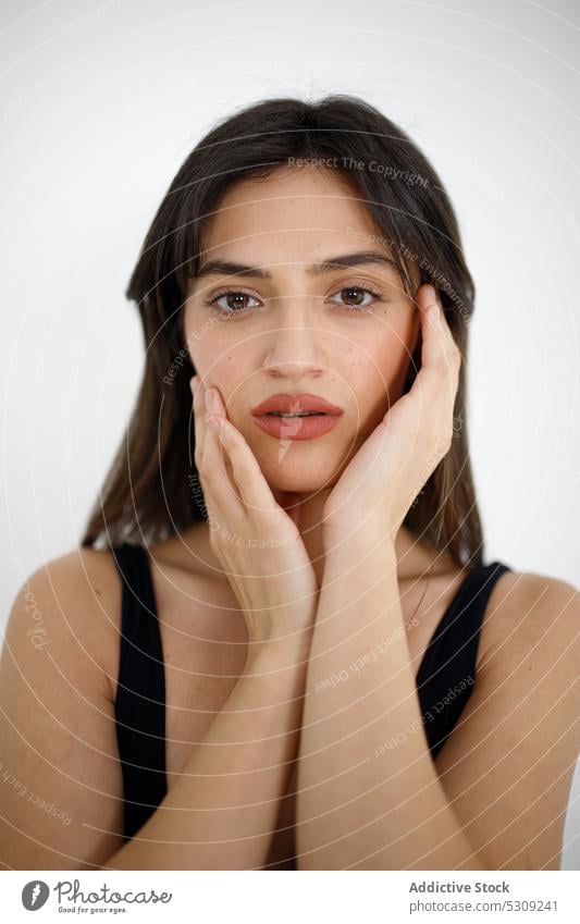 Attraktive Frau berührt Wangen im Studio Porträt Model Gesicht berühren Vorschein feminin Individualität jung dunkles Haar Make-up Persönlichkeit brünett Stil