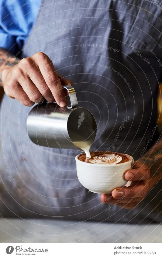 Crop Barista gießt Milch in Cappuccino im Café Mann Kaffee vorbereiten eingießen melken schäumen Bierschaum Latte männlich Kaffeehaus Latte Art Tasse Koffein