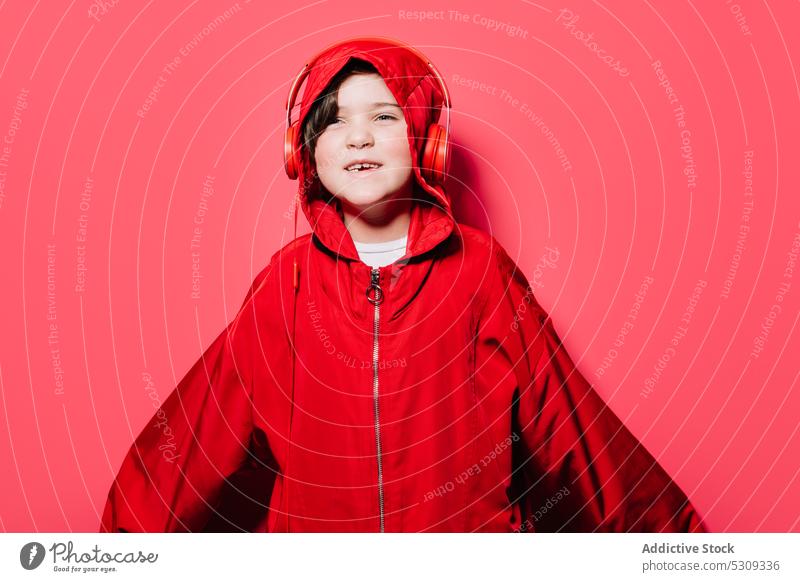 Glückliches junges Mädchen in übergroßem Regenmantel mit Kapuze im Studio lässig Kindheit Kopfhörer selbstbewusst Headset farbenfroh Lächeln modern Freude