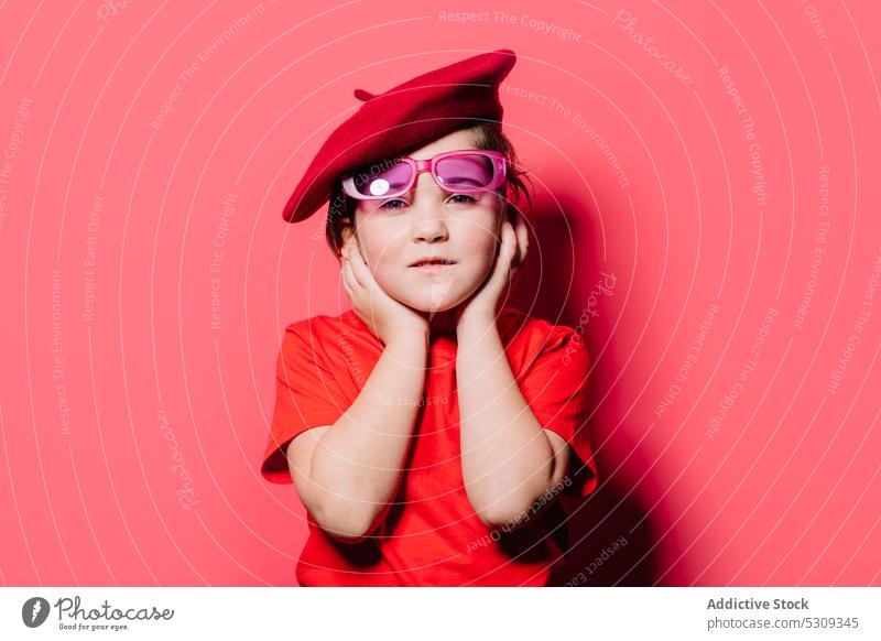 Niedliches kleines Mädchen in roter Freizeitkleidung mit Brille und Baskenmütze posiert im Studio traurig Stil Kind trendy Mode Sonnenbrille Outfit Model
