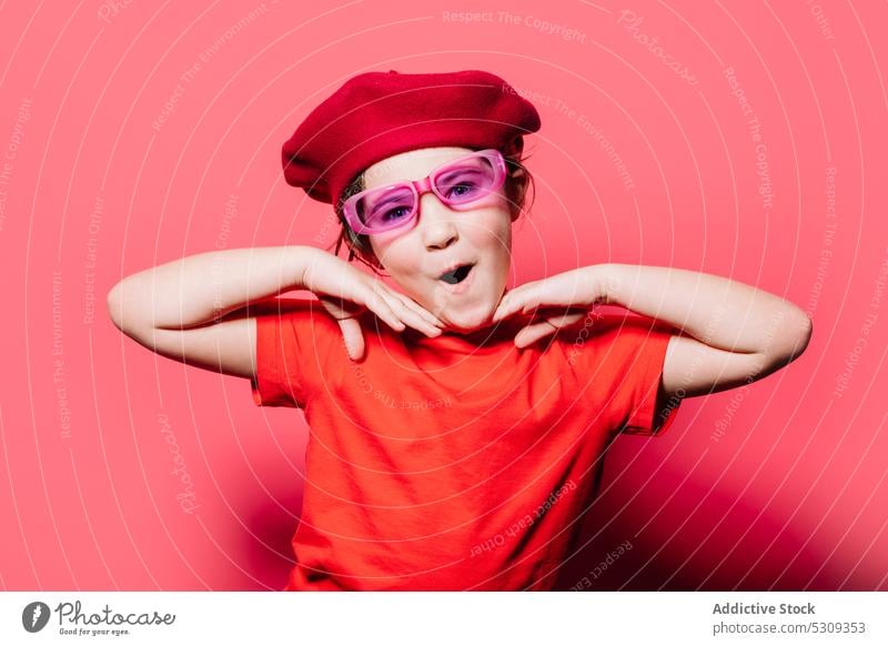 Lustiges Mädchen in rotem Freizeithemd und Baskenmütze in Superhelden-Pose, während sie in die Kamera schaut Stil Überraschung lässig Kind trendy Outfit Mode