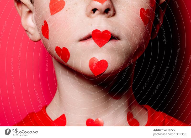Anonymer niedlicher Junge in rotem Freizeithemd mit rotem Liebesaufkleber im Gesicht beim Posieren für ein Foto Kind Atelier Aufkleber lässig modern bezaubernd