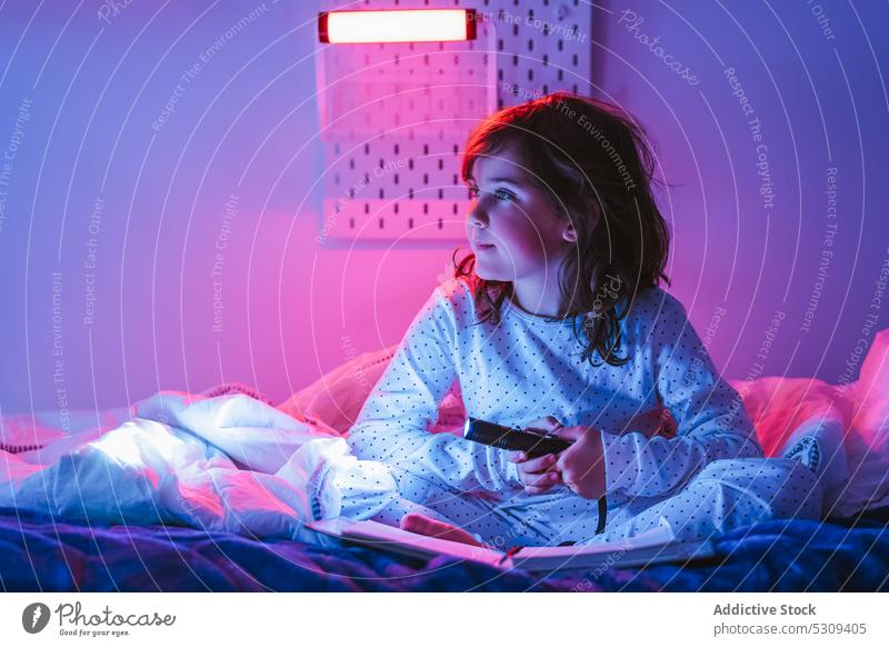Entzückendes Mädchen benutzt nachts eine Taschenlampe auf dem Bett Buch neugierig Nacht Beine gekreuzt Schlafzimmer Etage Kind Interesse leuchten lesen