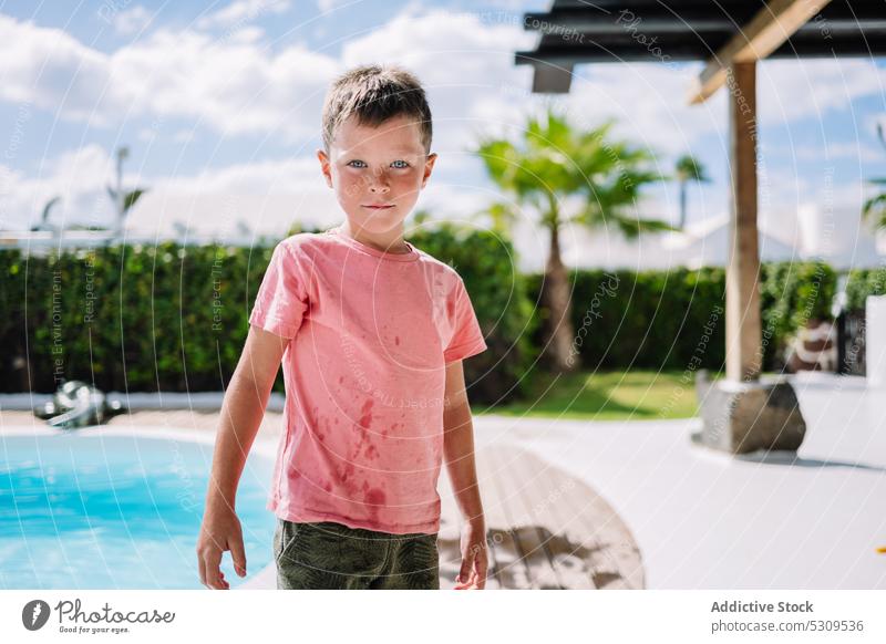 Niedlicher Junge in nasser Kleidung in der Nähe des Pools schaut in die Kamera Sommer Beckenrand Resort Feiertag Urlaub Kind ruhen Wasser Kindheit bezaubernd